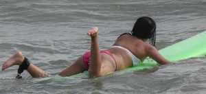 Brunette bikini girl on the beach and surfing in her bikini