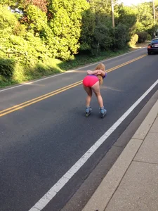 Girl in pink mini shorts bending over while skating on her roller blades down the road