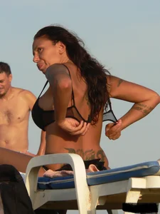 Topless tattooed lady on the beach with fake big tits