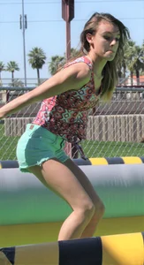 Brunette skinny teen in green shorts playing in a bounce house