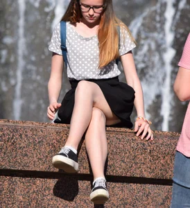 Teen Sitting On the City Fountain in a Skirt with Her Legs Crossed