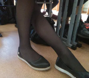 Feet in Flats and Black Pantyhose Under the College Desk in Classroom Closeup Photo