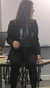 Teen GIrl in a School Uniform Sitting on Top of Desk in a Classroom Creepshot