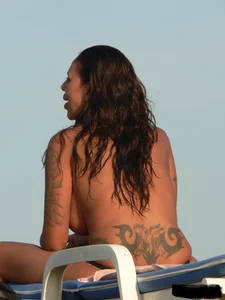 Topless tattooed lady on the beach with fake big tits