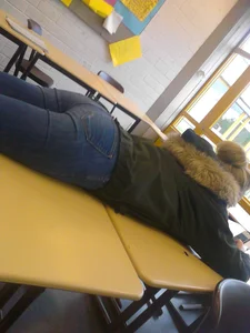 Teen In Tight Blue Jeans Lying on Top of Desk in Class