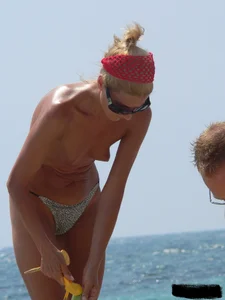 Topless skinny blonde lady in a g-string bikini at the beach