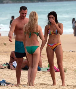 Sexy brunette in thong bikini and blonde friend in green bikini at the beach
