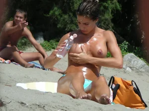 Brunette on the beach takes her top off and oils her nice tits