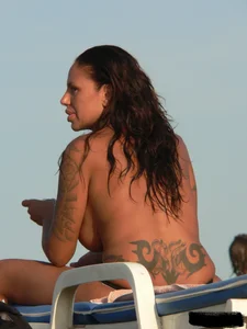 Topless tattooed lady on the beach with fake big tits