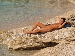 Naked nudist girl lying by the water