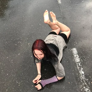 Teen with red wet hair lying on asphalt, wet after rain