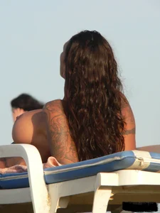 Topless tattooed lady on the beach with fake big tits